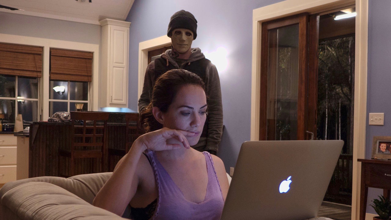 Um assassino mascarado observa Kate Siegel trabalhando em uma cena de “Hush”.