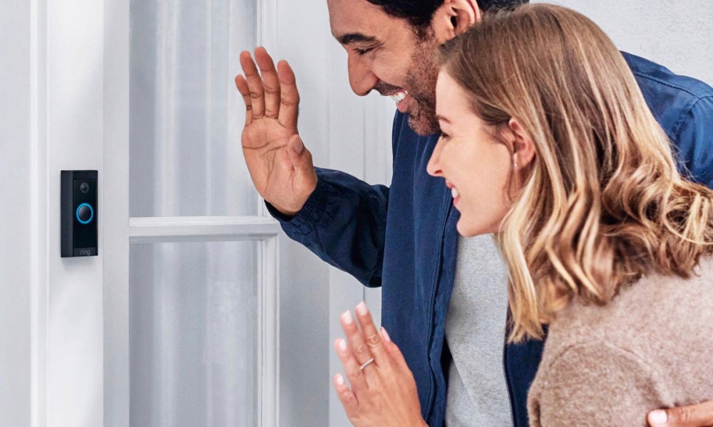 Two people waving in front of a Ring Video Doorbell Wired