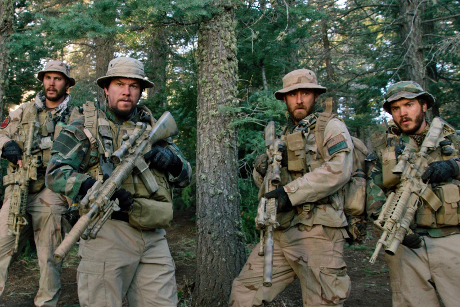 Four soldiers hold guns in the mountains.