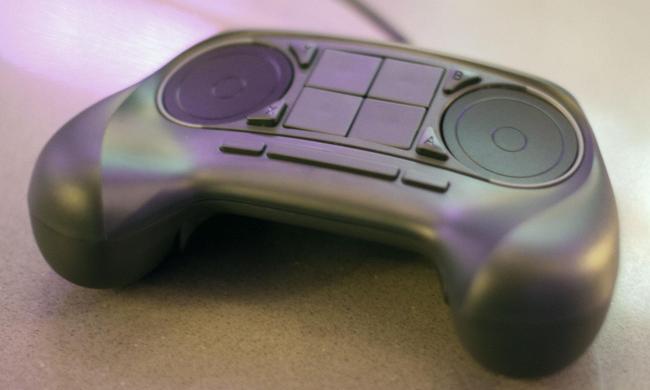 A Steam Controller from Valve on a surface. You can see two track pads on top with four buttons in the middle.