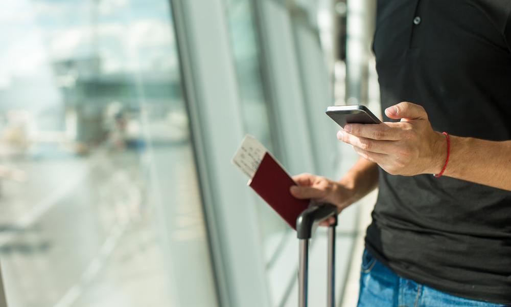 Man at airport with iPhone and airline ticket in hand.