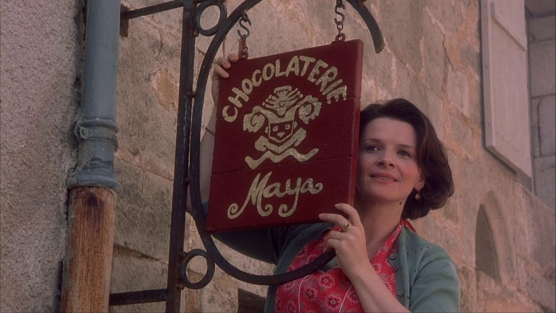 Juliette Binoche as Vianne hanging a sign and smiling in Chocolat.