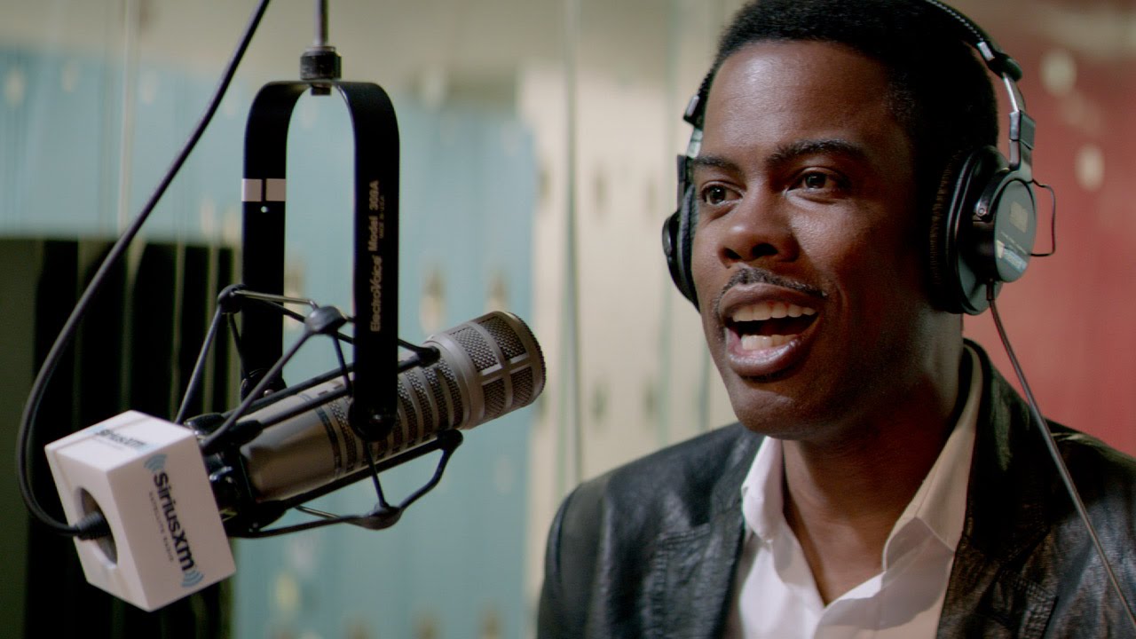 Chris Rock está sentado atrás de um microfone no Top Five.