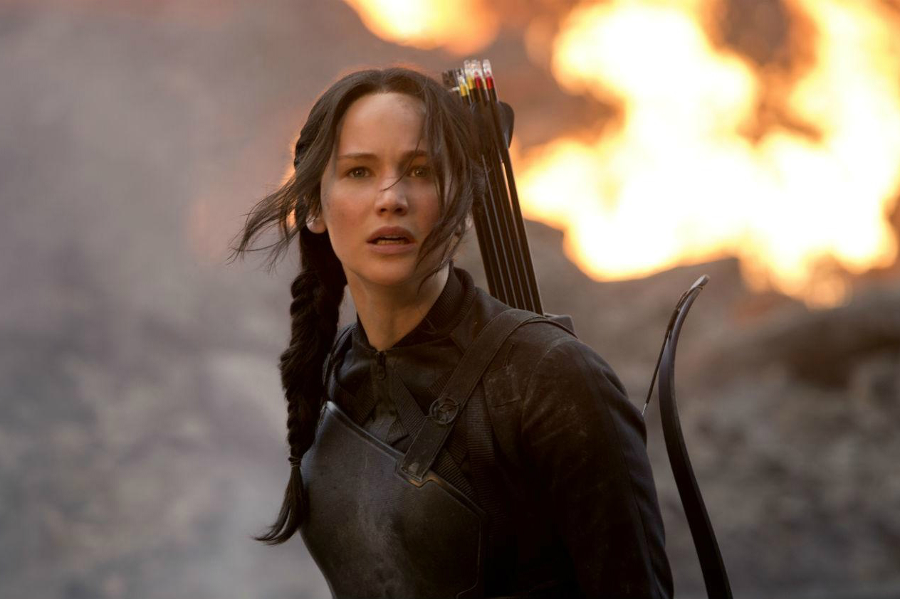 Jennifer Lawrence stands and stares with fire behind her in The Hunger Games.