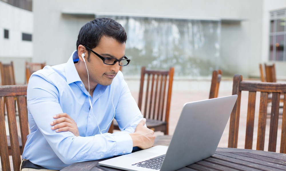 A person sitting at a table and watching something on a laptop.