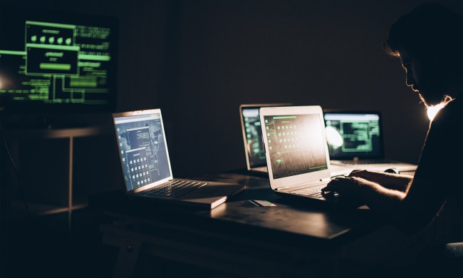 An individual surrounded by several computers typing on a laptop.