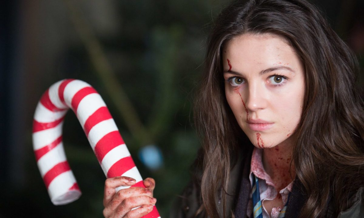 Ella Hunt as Anna holding a large candy cane and looking at the camera in Anna and the Apocalypse.