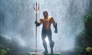 Aquaman standing in front of a waterfall holding a trident in the movie "Aquaman."