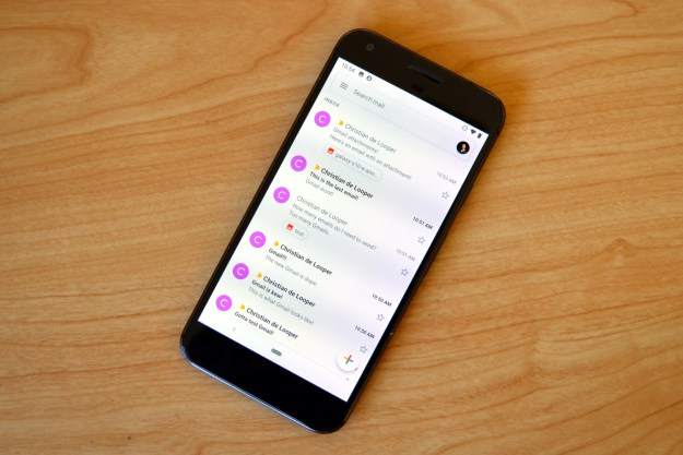 A smartphone sitting on a wooden table, showing the Gmail app's inbox on its screen.