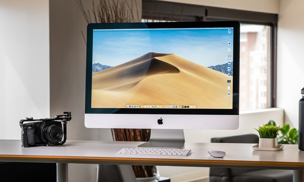 An Apple iMac from 2019 placed on a desk. The macOS Mojave operating system is on its display.