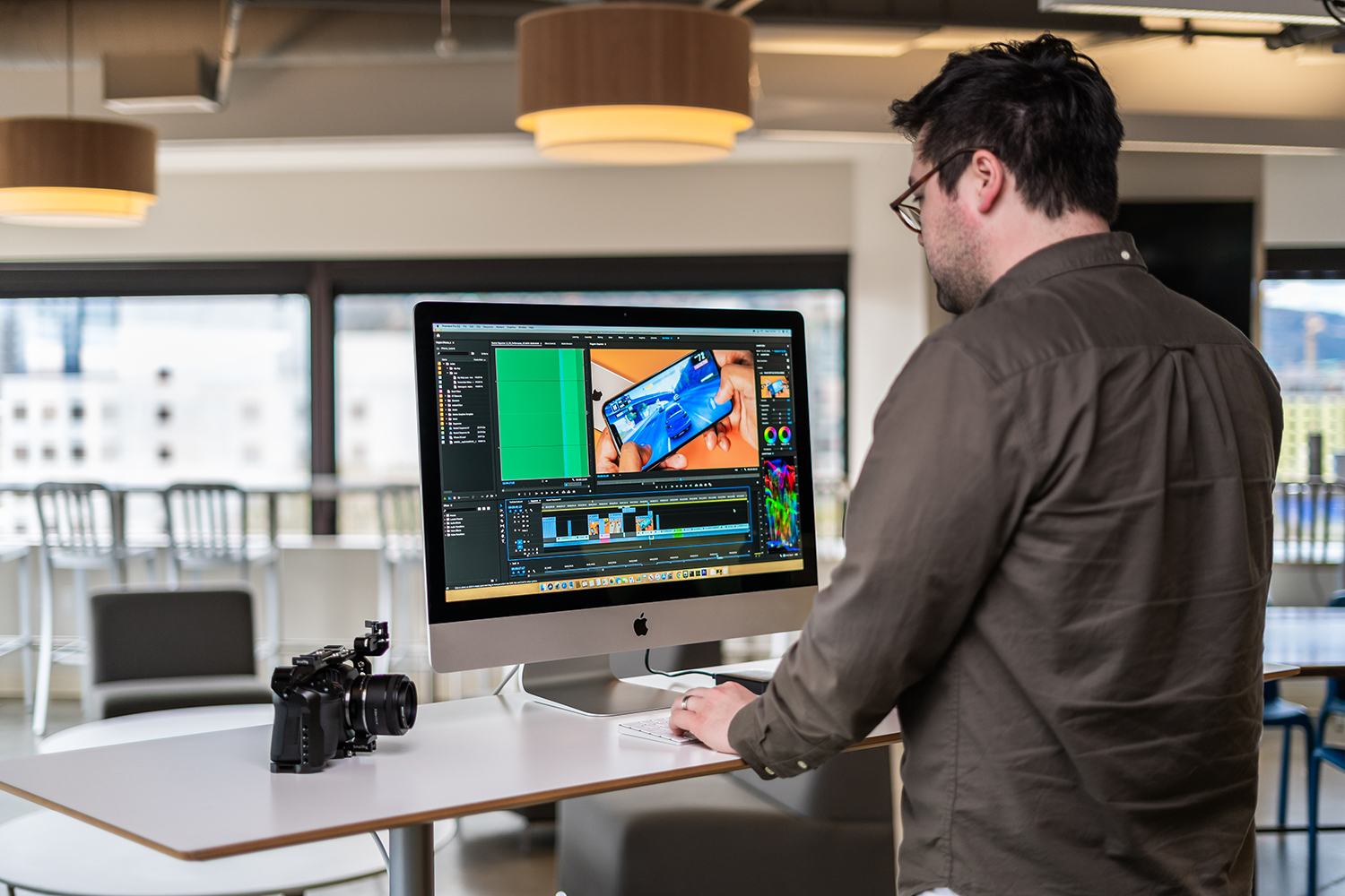 A man standing in front of an iMac with a camera on the desk.