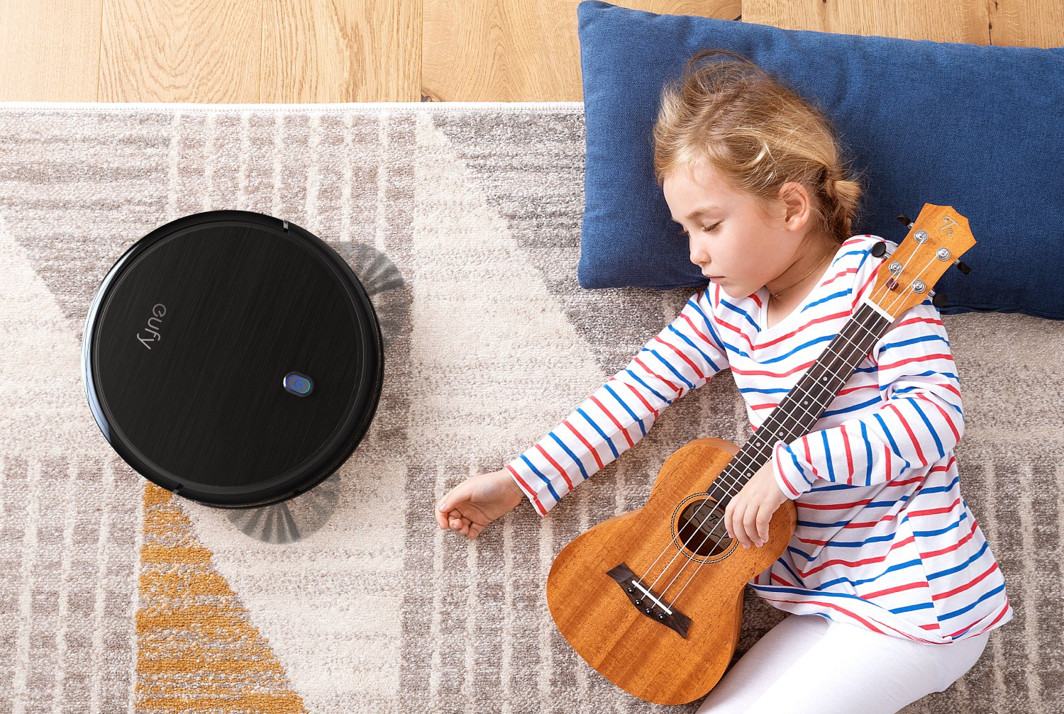 Un aspirateur robot Eufy sur un tapis près d'un jeune enfant qui fait la sieste sur le sol.