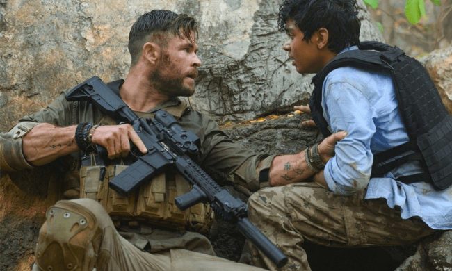 Chris Hemsworth holds a kid and a gun in Extraction.