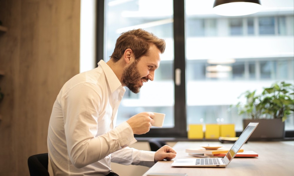 A man holding a teacup staring at laptop screen.