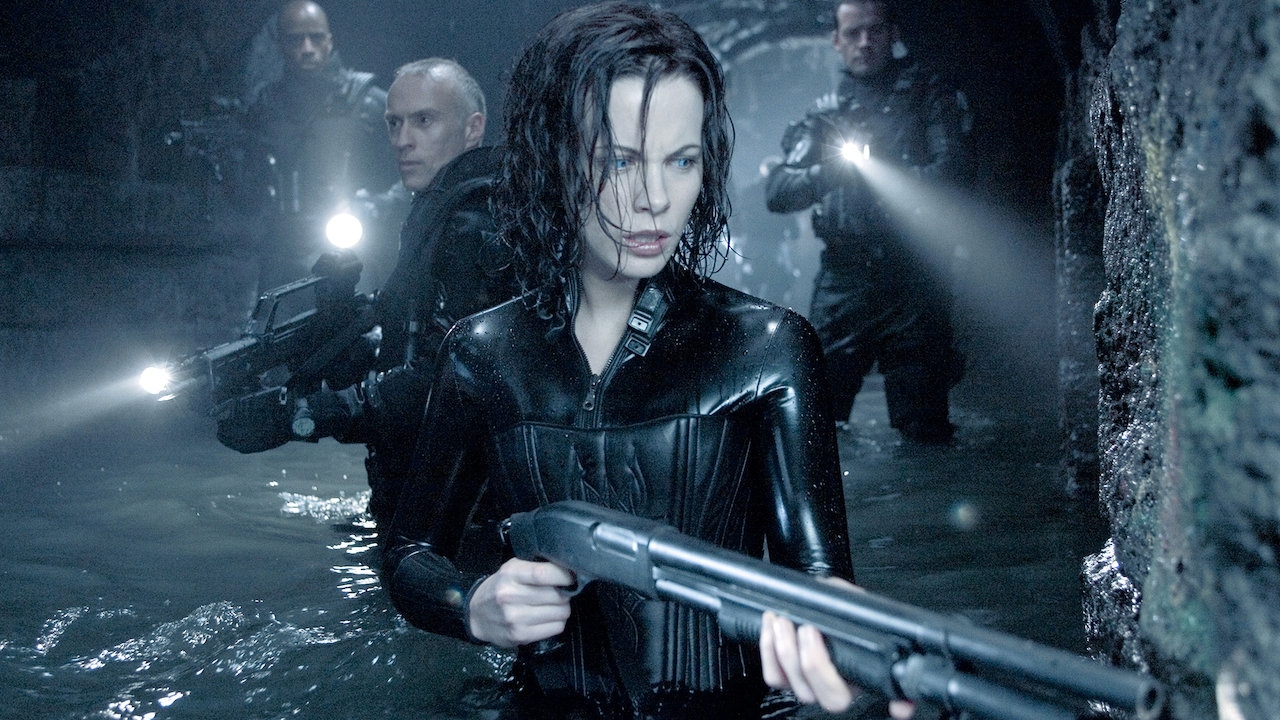 Kate Beckinsale como Selene sosteniendo un arma seguida por dos hombres en Underworld