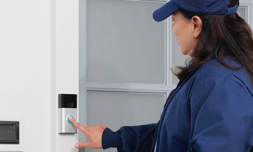 The Ring Video Doorbell on a door frame while a woman touches it.