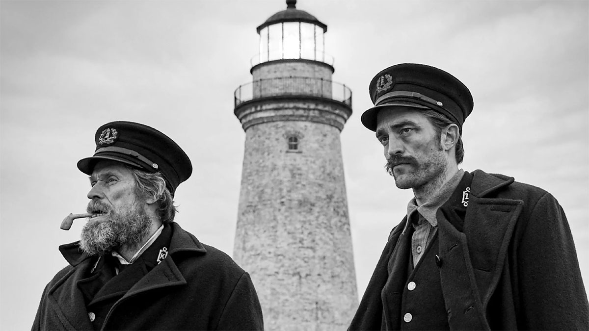 Willem Dafoe et Robert Pattinson en personnage avec un phare en arrière-plan dans The Lighthouse.