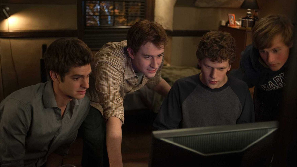 Andrew Garfield, Joseph Mazzello, and Jesse Eisenberg as Eduardo Saverin, Dustin Moskovitz, and Mark Zuckerberg looking at a computer monitor in The Social Network.