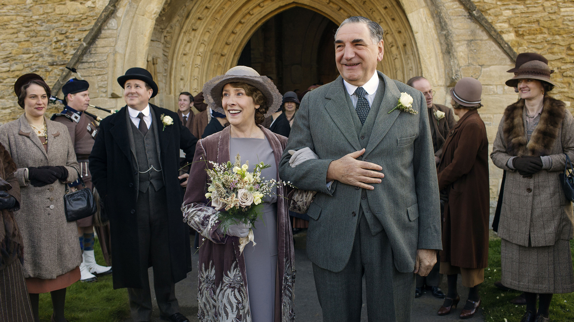 Un homme et une femme marchent main dans la main sous les yeux d’une foule à Downton Abbey.