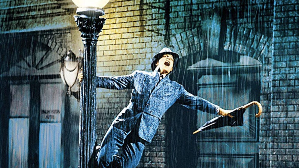 Gene Kelly como Don Lockwood cantando bajo la lluvia mientras sostiene un poste de luz en Cantando bajo la lluvia (1952)