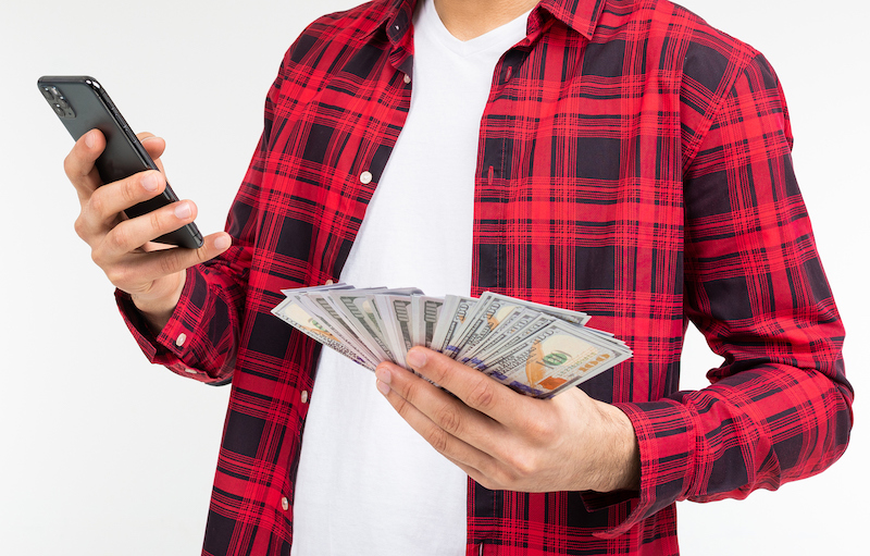 retrato de un chico lindo con un montón de dinero hablando por teléfono sobre un fondo de estudio blanco con espacio para copiar