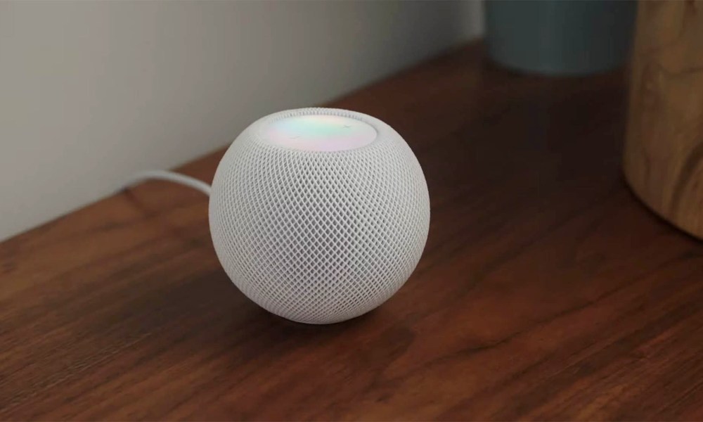 A white HomePod mini sitting on a desk.