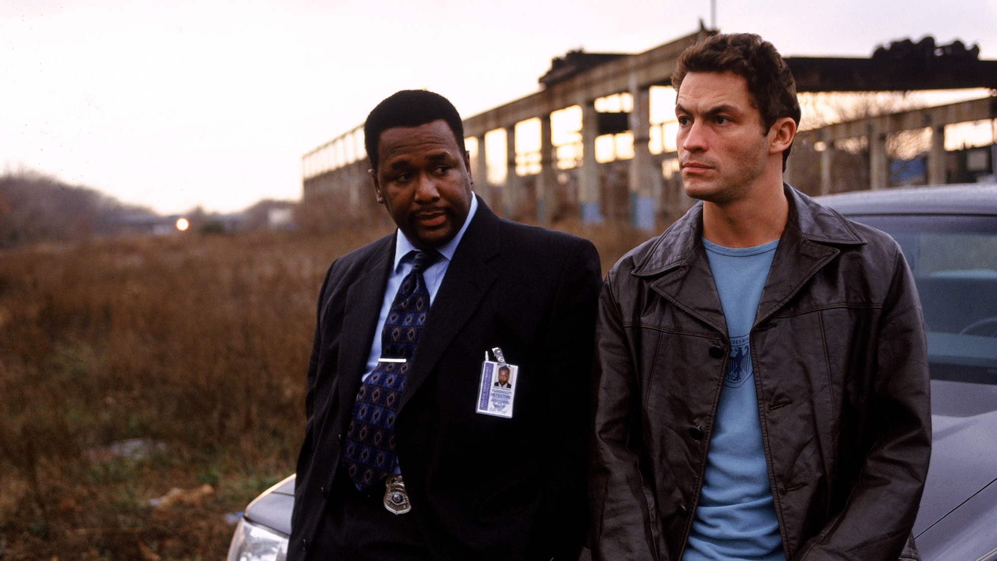 Twee personages uit The Wire leunend tegen een auto.