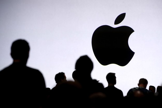 Apple logo on screen in front of group of people.