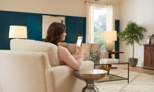 A woman sitting on her couch looking at the Hubspace app on her phone.