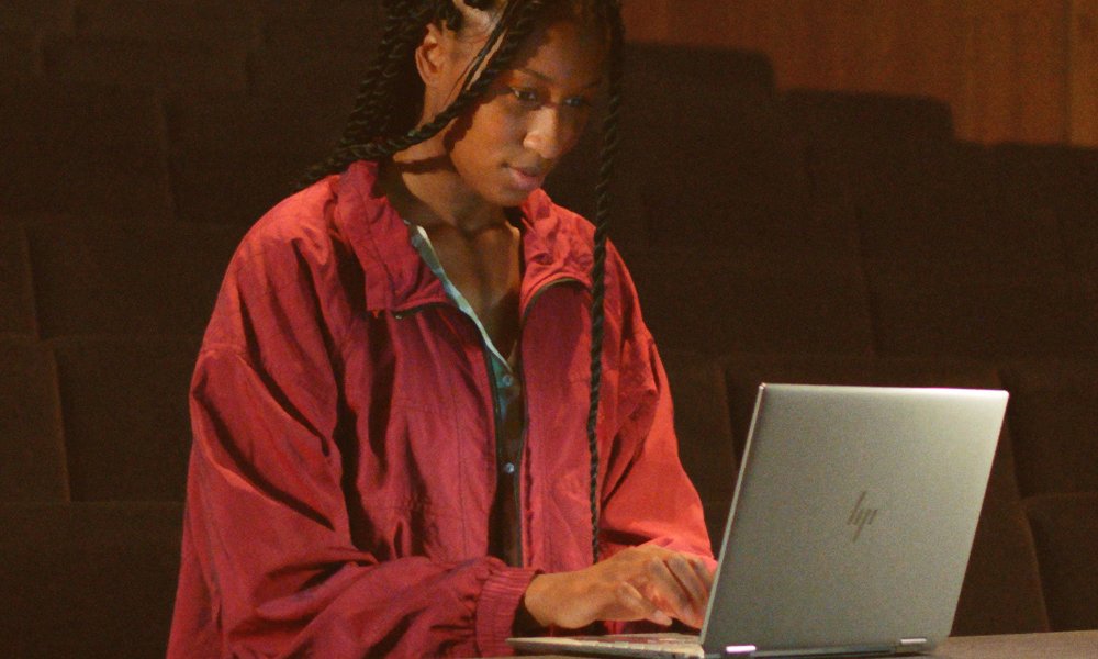 A woman sitting at a desk looking at the HP Envy x360.