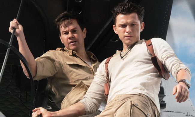 Tom Holland and Mark Wahlberg stand on the edge of a plane and stare down.