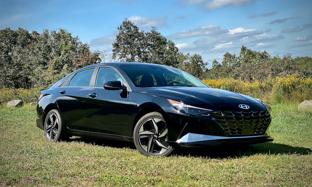 Angled front view of the 2021 Hyundai Elantra Hybrid Platinum in a grassy field (passnger's side).