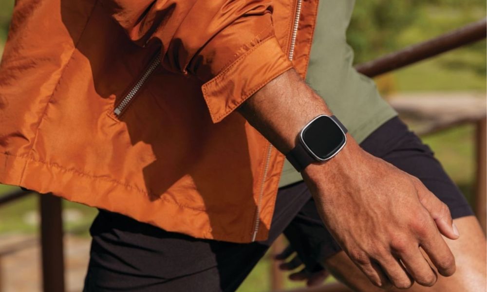 The Fitbit Sense on a man's wrist while he walks outdoors.