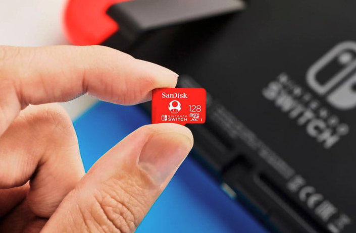 Une main tient une carte mémoire microSDXC SanDisk de 128 Go pour Nintendo Switch de près avec la console en arrière-plan.