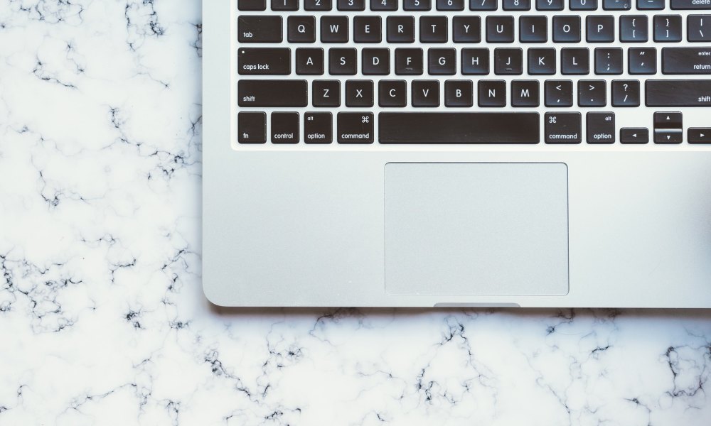 Open MacBook, keyboard on a marble desk.