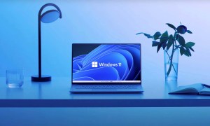 A laptop sits on a desk with a Windows 11 wallpaper.