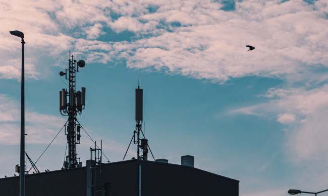 Cellular radio towers on roof of building against sky with clouds.