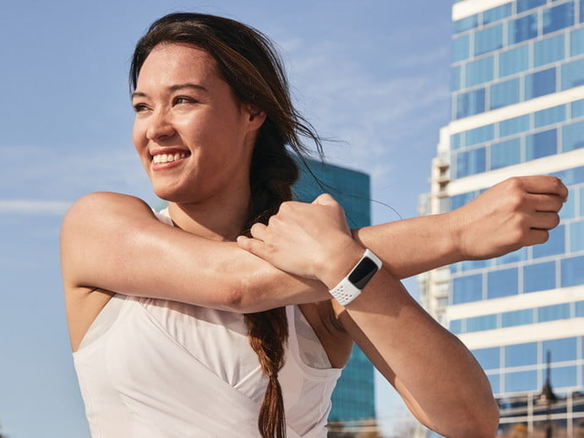 A woman wearing a Fitbit Charge 5 stretching her shoulder during a workout.