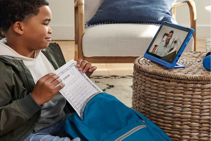 Ein kleiner Junge mit einem Arbeitsblatt, der sich ein Video auf einem blauen Amazon Fire HD 10 Kids Pro-Tablet ansieht.