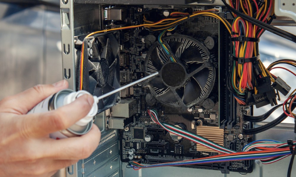 A compressed air can being aimed towards the inside of a PC to remove dust.