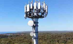 Large 5G cellular tower with multiple mmWave transceivers against a blue sky.