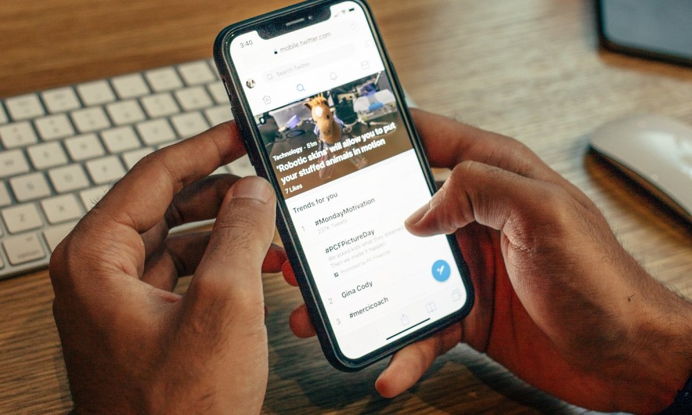 A person's hands holding a smartphone as they browse Twitter on it.