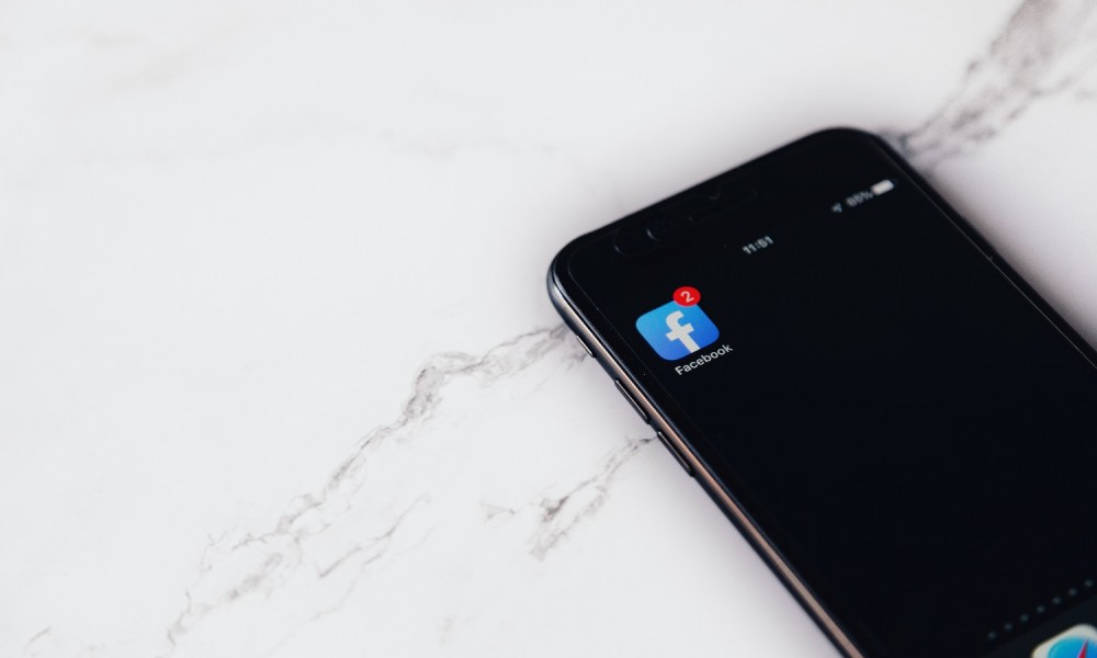 A smartphone with the Facebook app icon on it all on a white marble background.