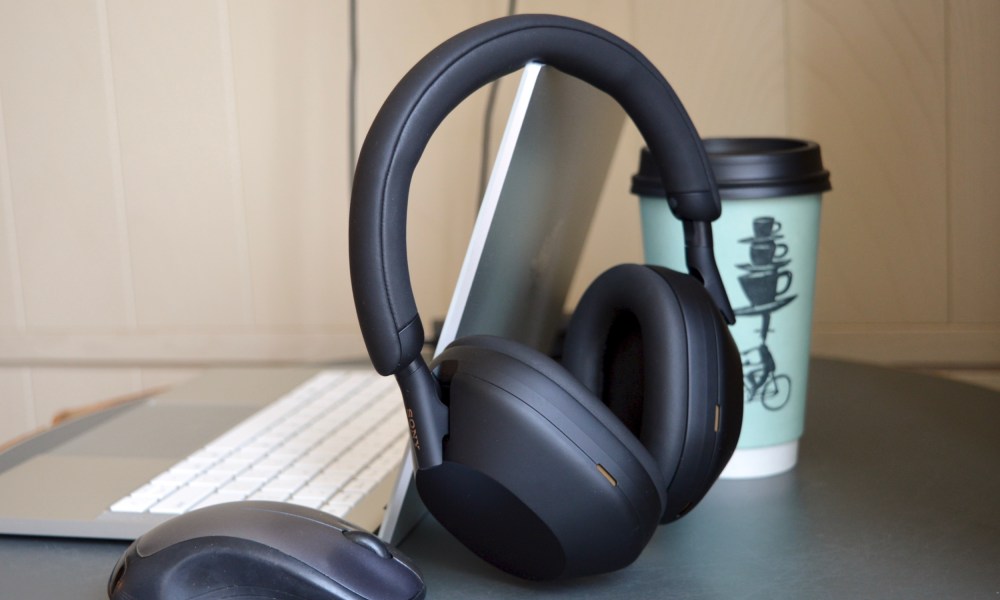 Sony WH-1000XM5 wireless headphones next to a laptop, mouse, and coffee cup.