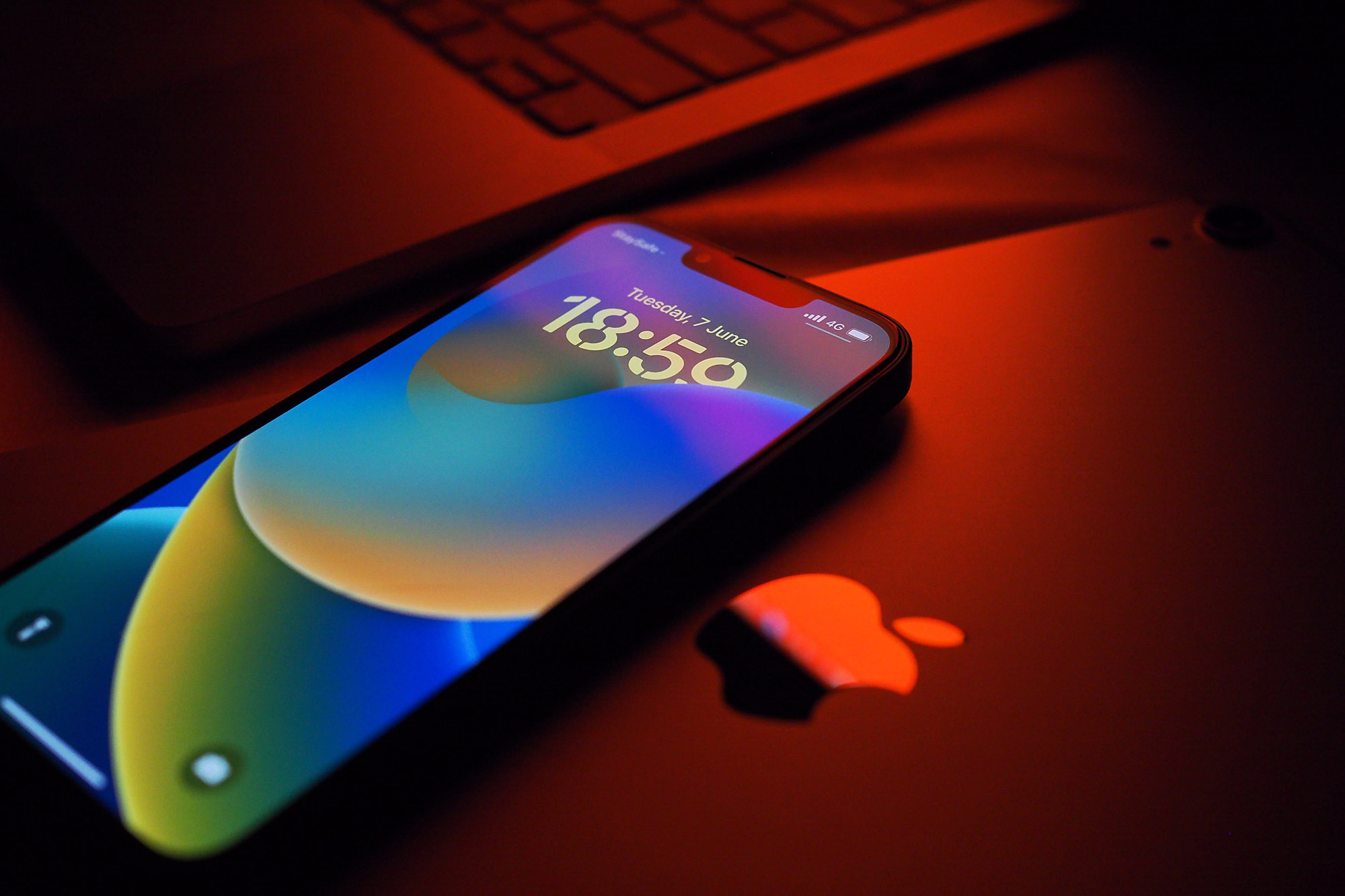 An iPhone 13 Pro running iOS 16 sits on top of an iPad with red lighting shining.