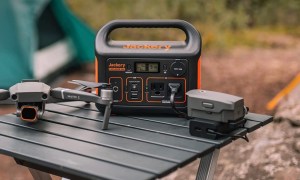 Jackery Portable Power Station Explorer 300 sits on a table at a camping site next to a drone.