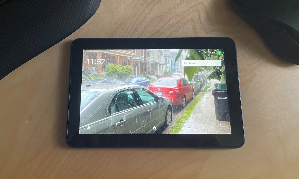 2022 amazon fire 7 laying on a desk next to a keyboard and mouse. Its display shows a rainy day.