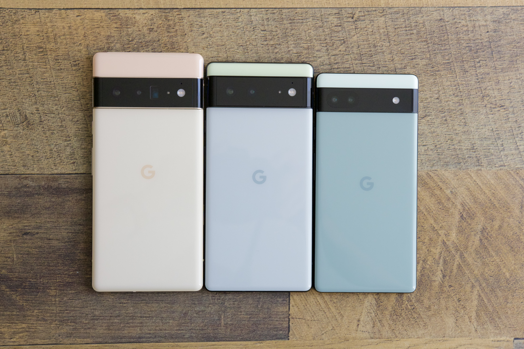 The Google Pixel 6 Pro, Pixel 6, and Pixel 6a all lined up on a wooden desk.