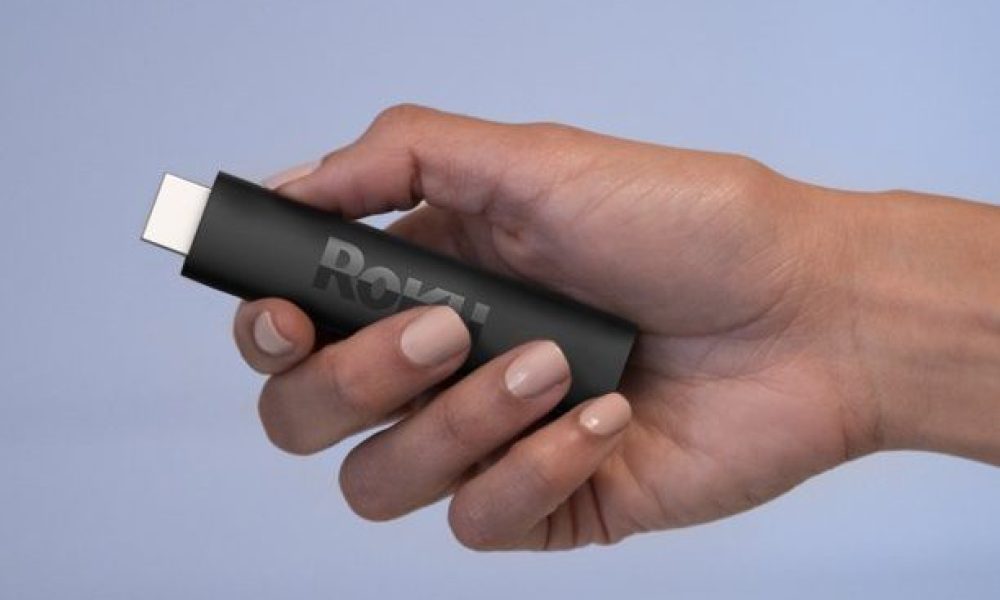 Hand holding a Roku Streaming Stick 4K on a grey background.