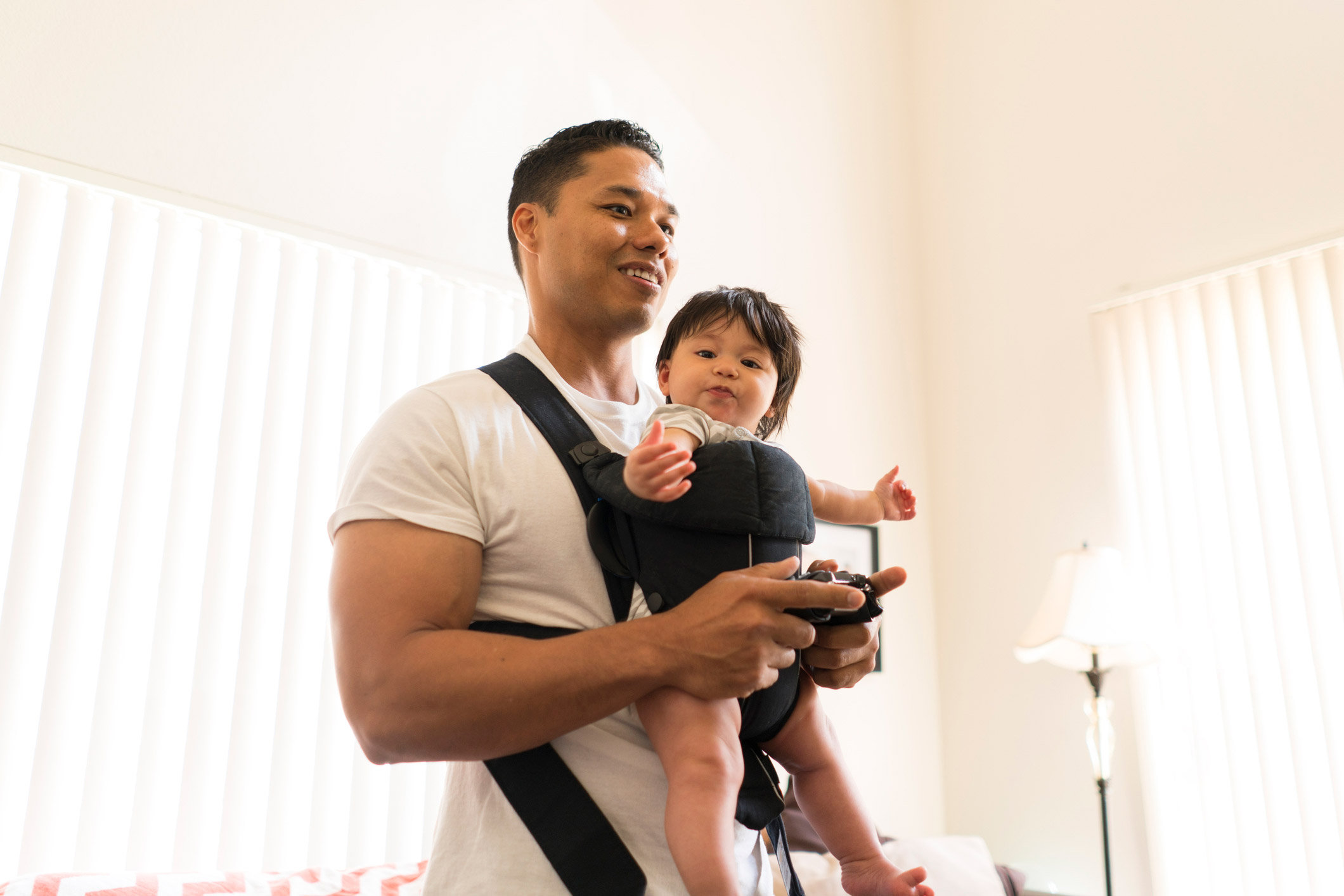 Um pai de pé e jogando com um bebê em uma transportadora.